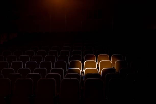 Empty theater with a single spotlight illuminating a few vacant seats in an otherwise dark auditorium.