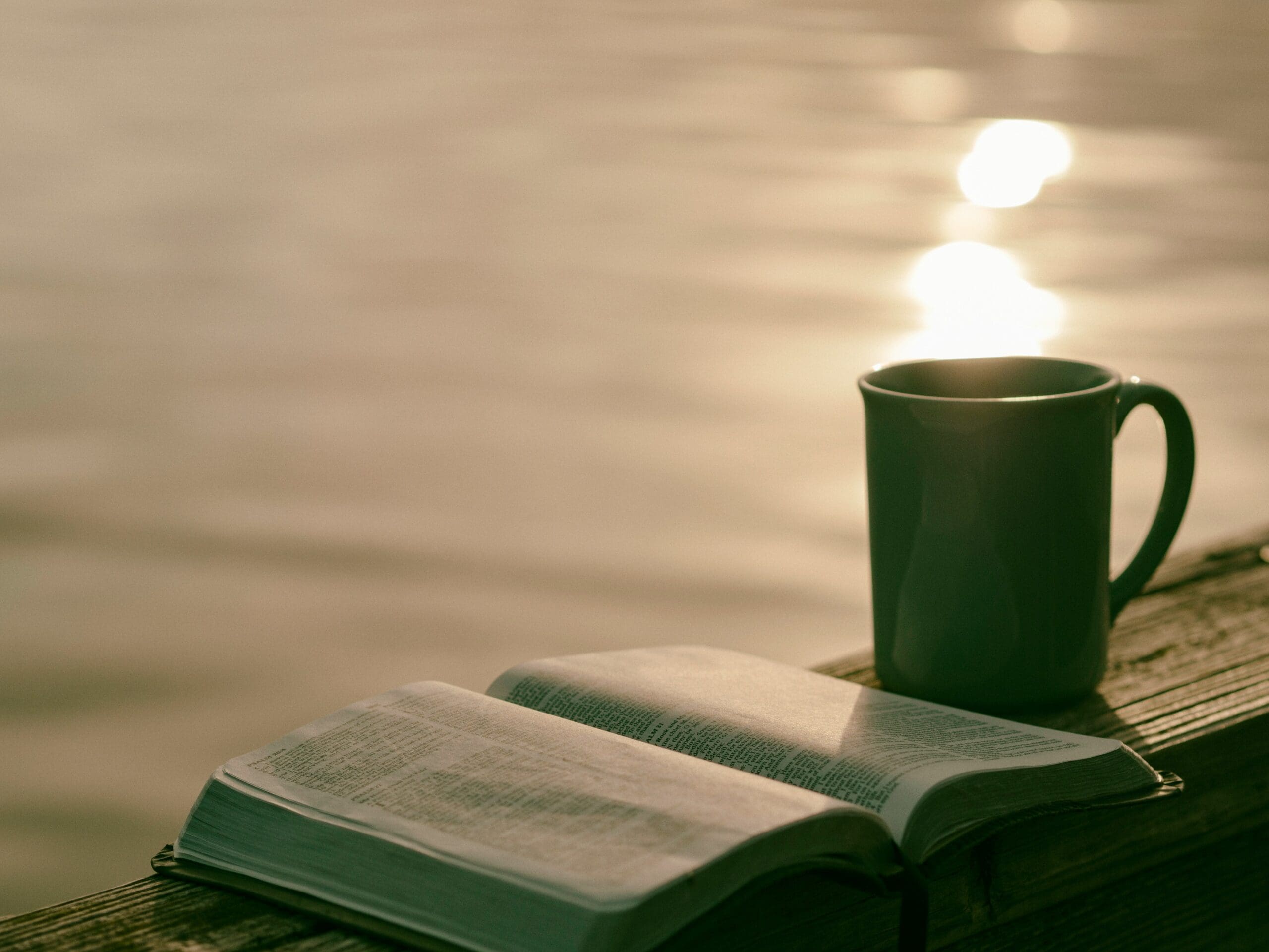 Open book and coffee mug on a wooden dock at sunrise over calm water