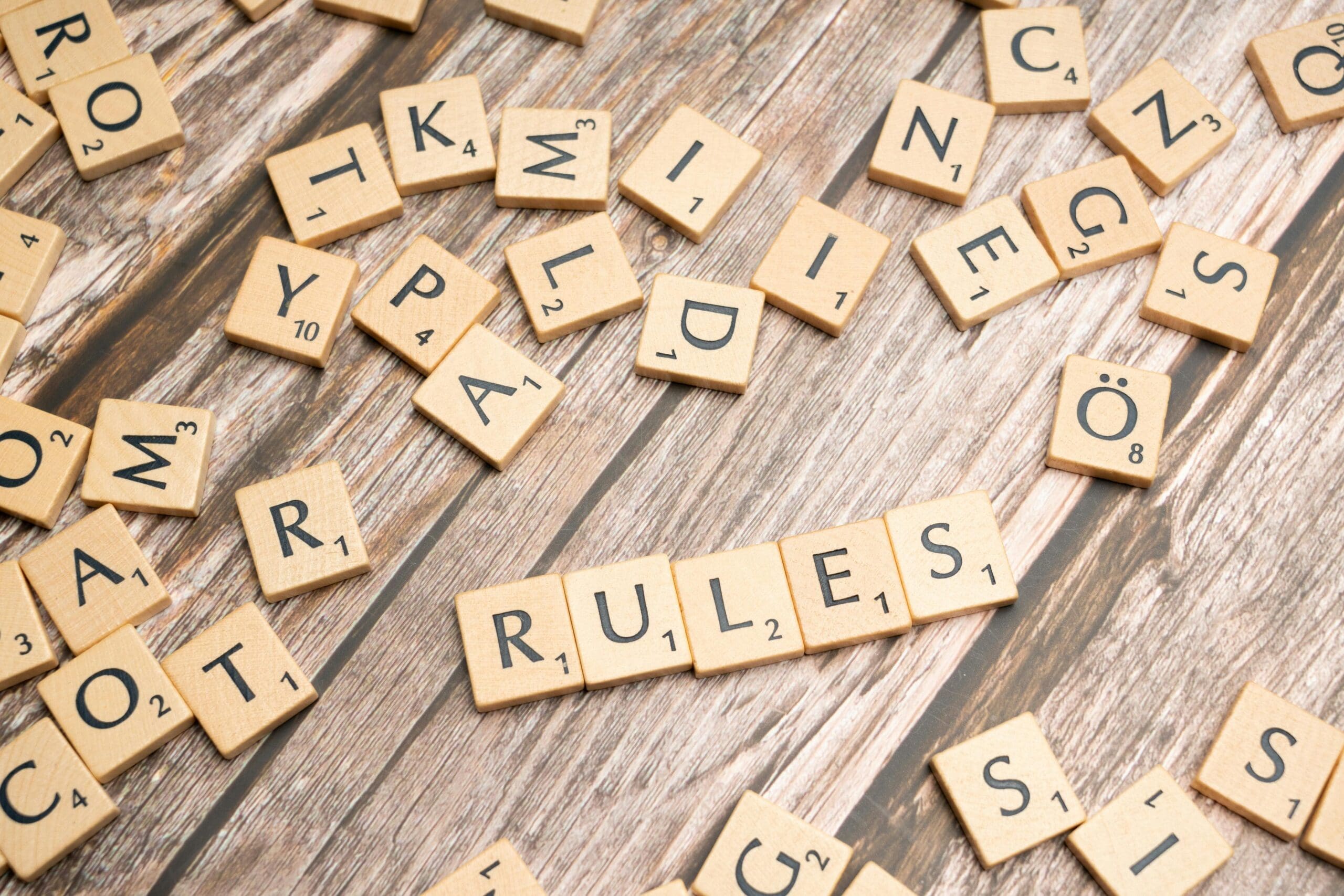 Scrabble tiles scattered on a wooden surface, with the word “RULES” spelled out in the center.