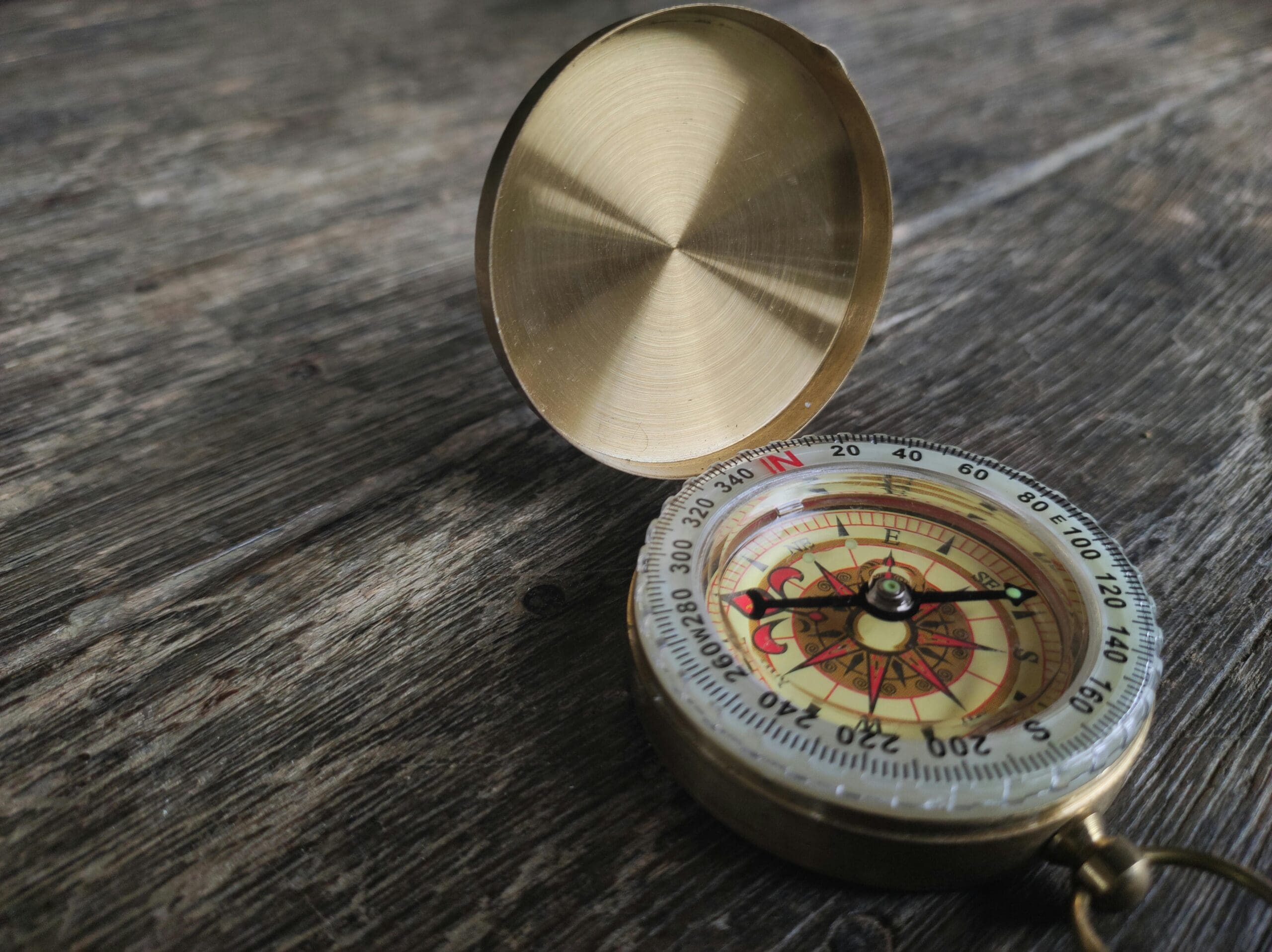 Vintage brass compass open on a weathered wooden surface, pointing north.
