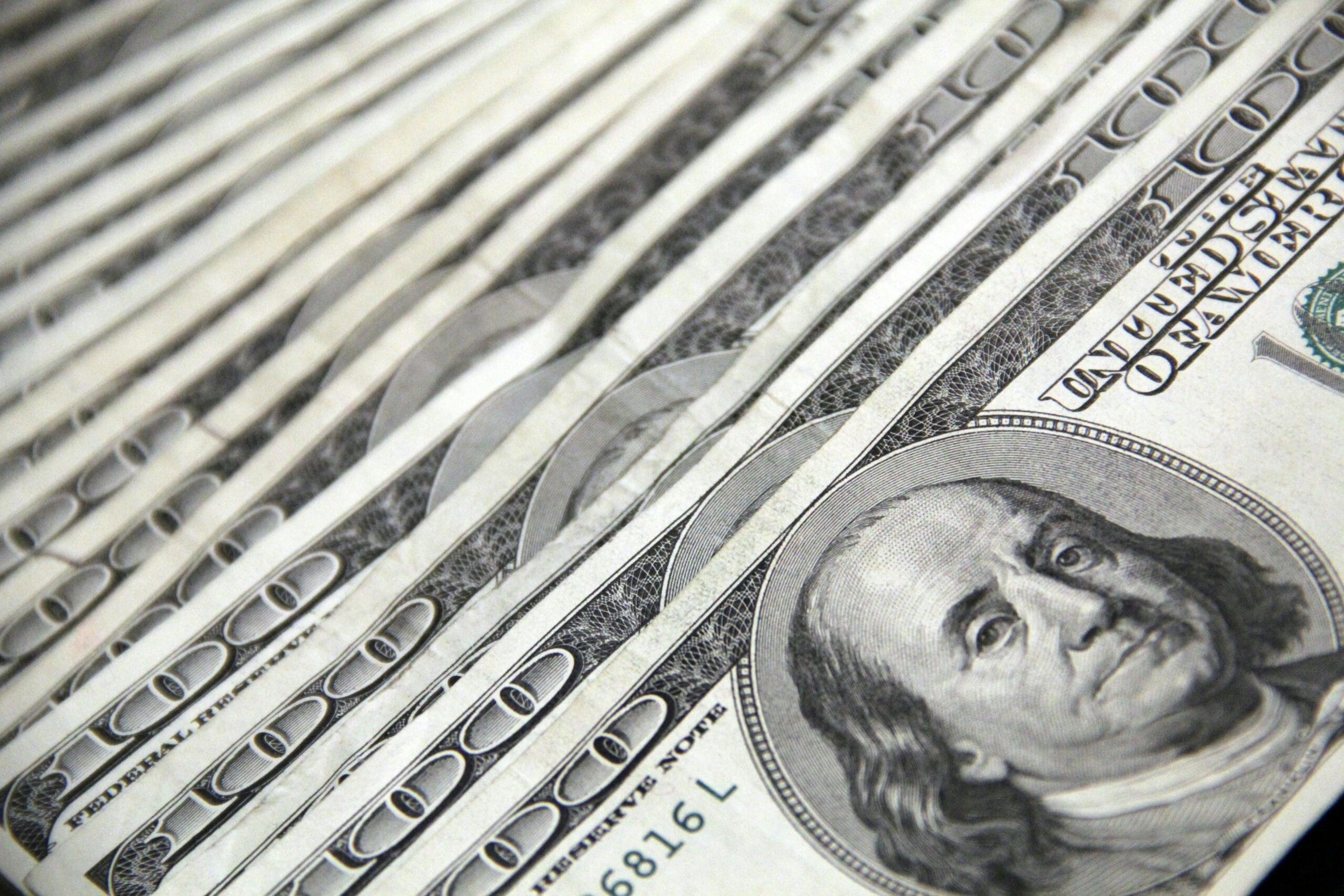 Stacked U.S. hundred-dollar bills fanned out in close-up, with Benjamin Franklin’s portrait visible