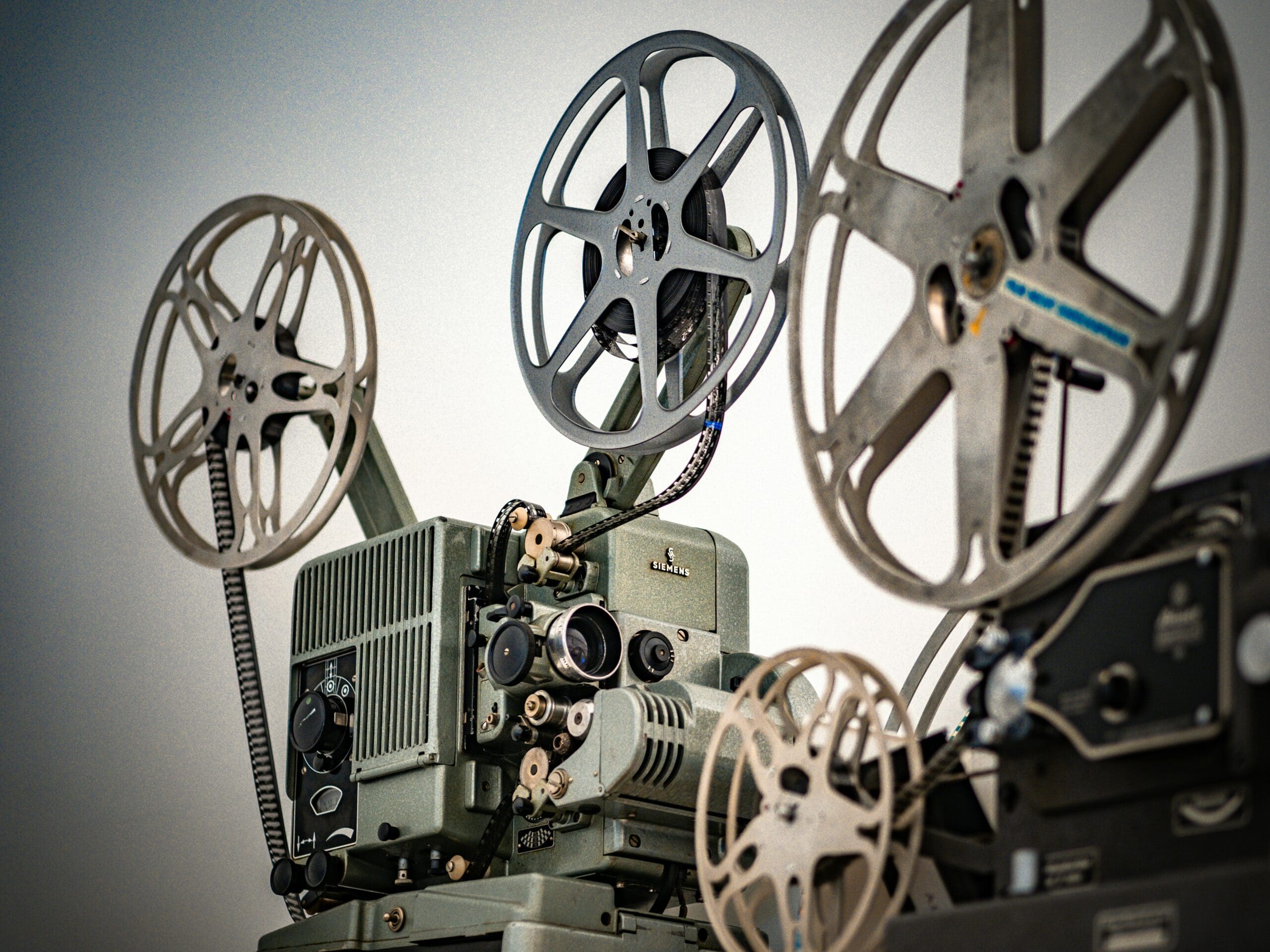Close-up of a vintage Siemens film projector with multiple film reels, set against a neutral background.