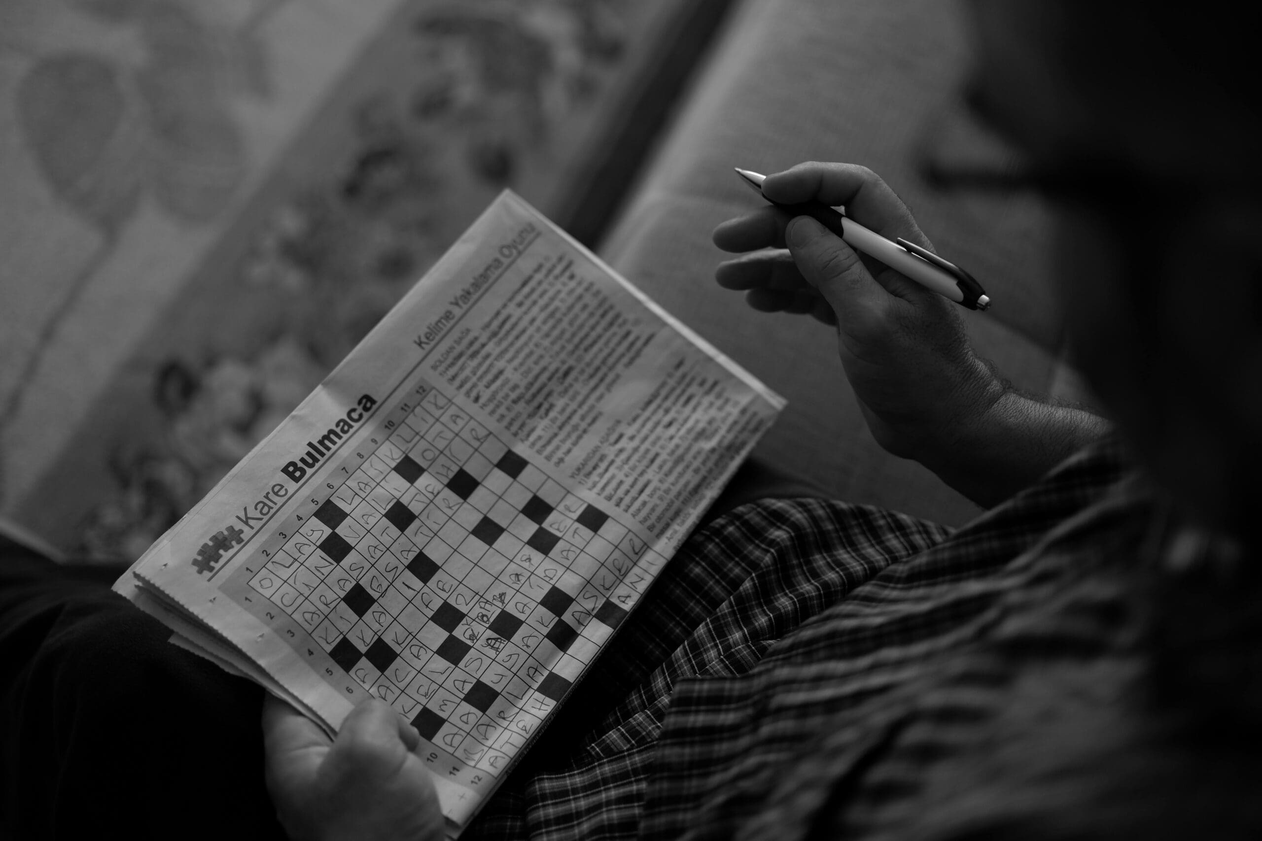 Person solving a crossword puzzle in a newspaper while holding a pen.