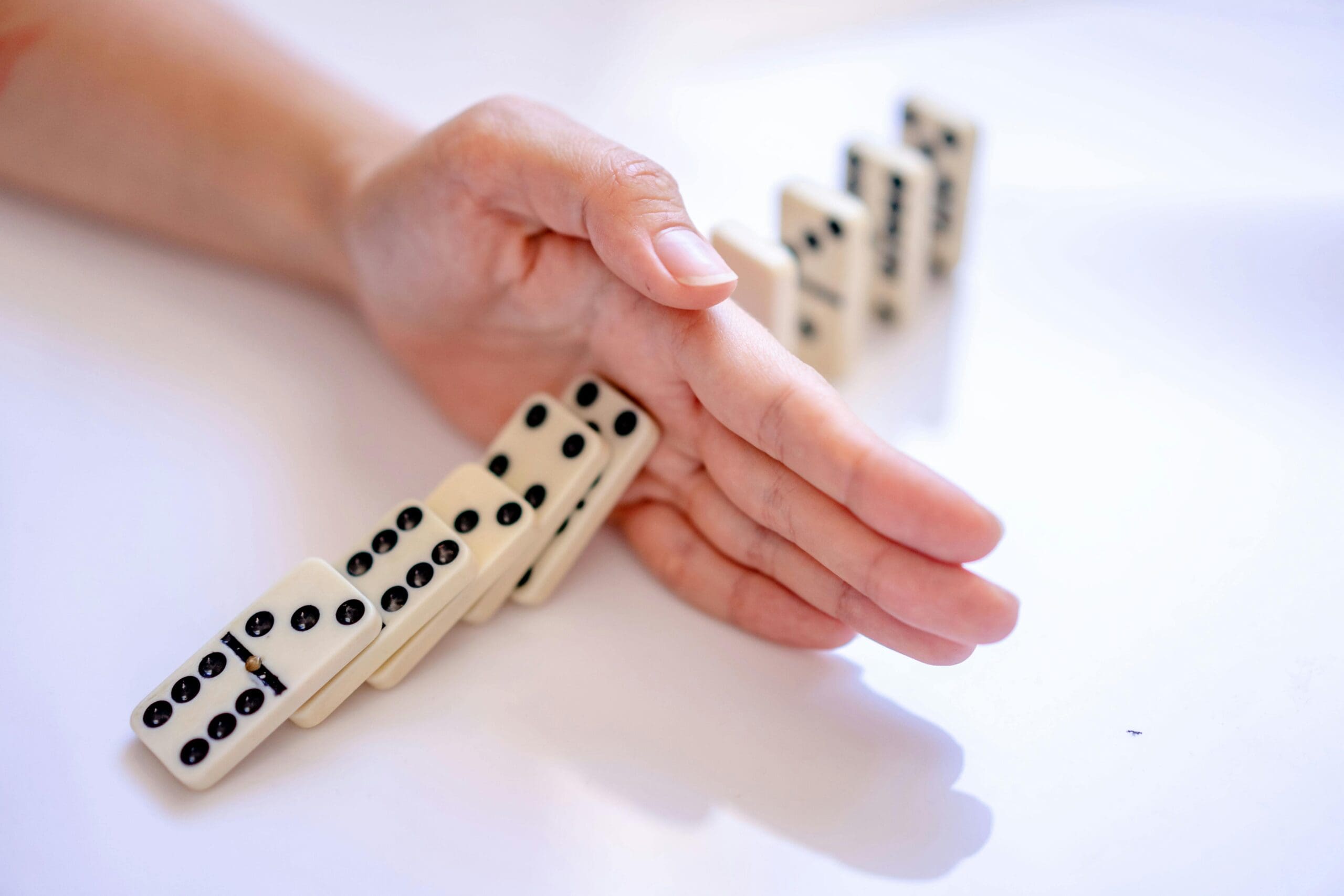 A human hand stopping a row of falling dominoes mid-collapse, preventing the remaining pieces from toppling.