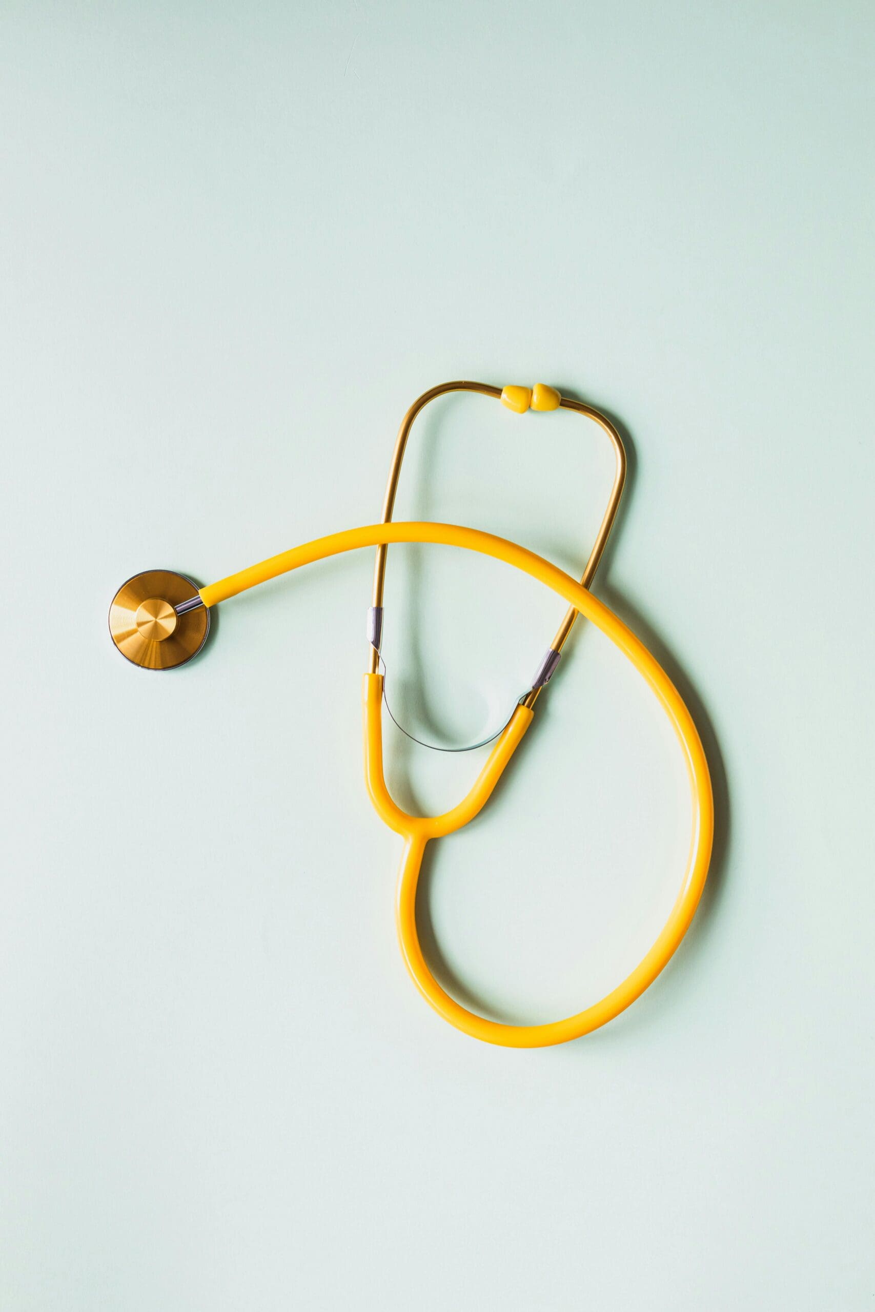 Yellow stethoscope lying on a light green background.