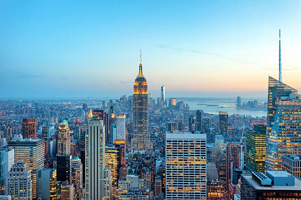 New York City skyline at sunset with the Empire State Building and surrounding skyscrapers illuminated against a clear evening sky.