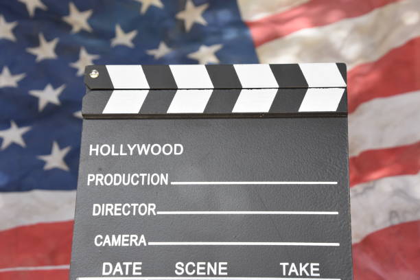 Hollywood film clapperboard in front of a blurred American flag backdrop.