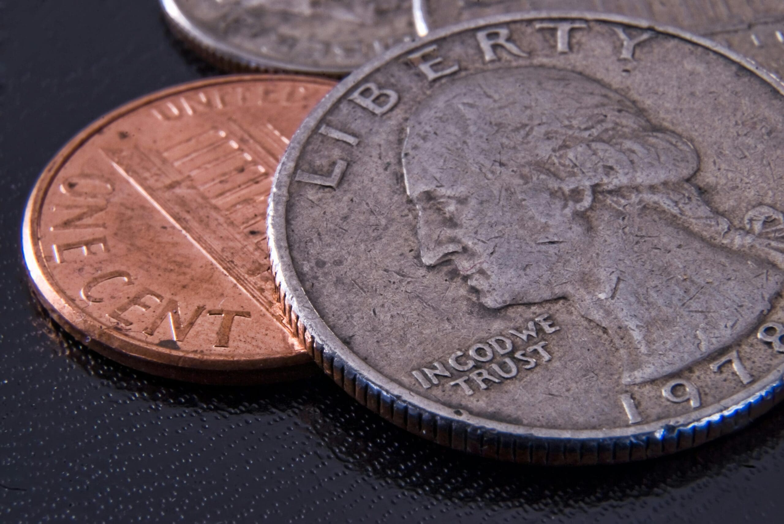 Macro close-up of a worn 1978 U.S. quarter overlapping a shiny copper penny on a dark textured surface.