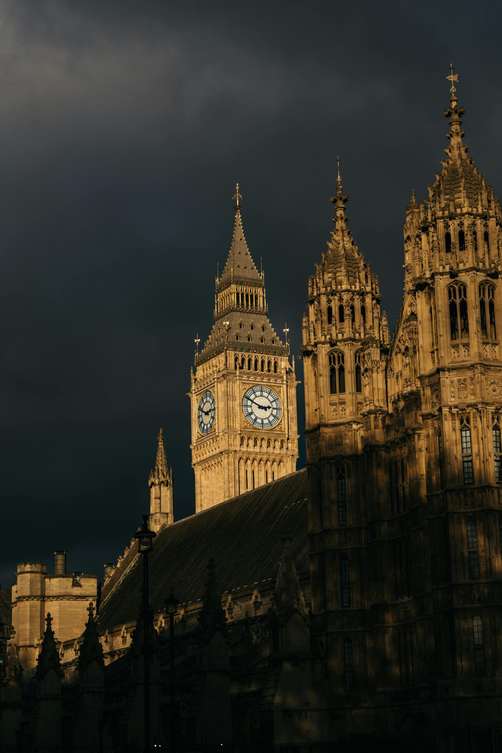 The Elizabeth Tower in London illuminated by warm sunset light against a dark, stormy sky.