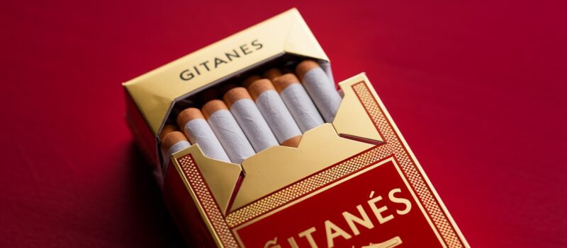 Open pack of Gitanes cigarettes on a red surface, showing unfiltered cigarettes associated with classic French café culture.