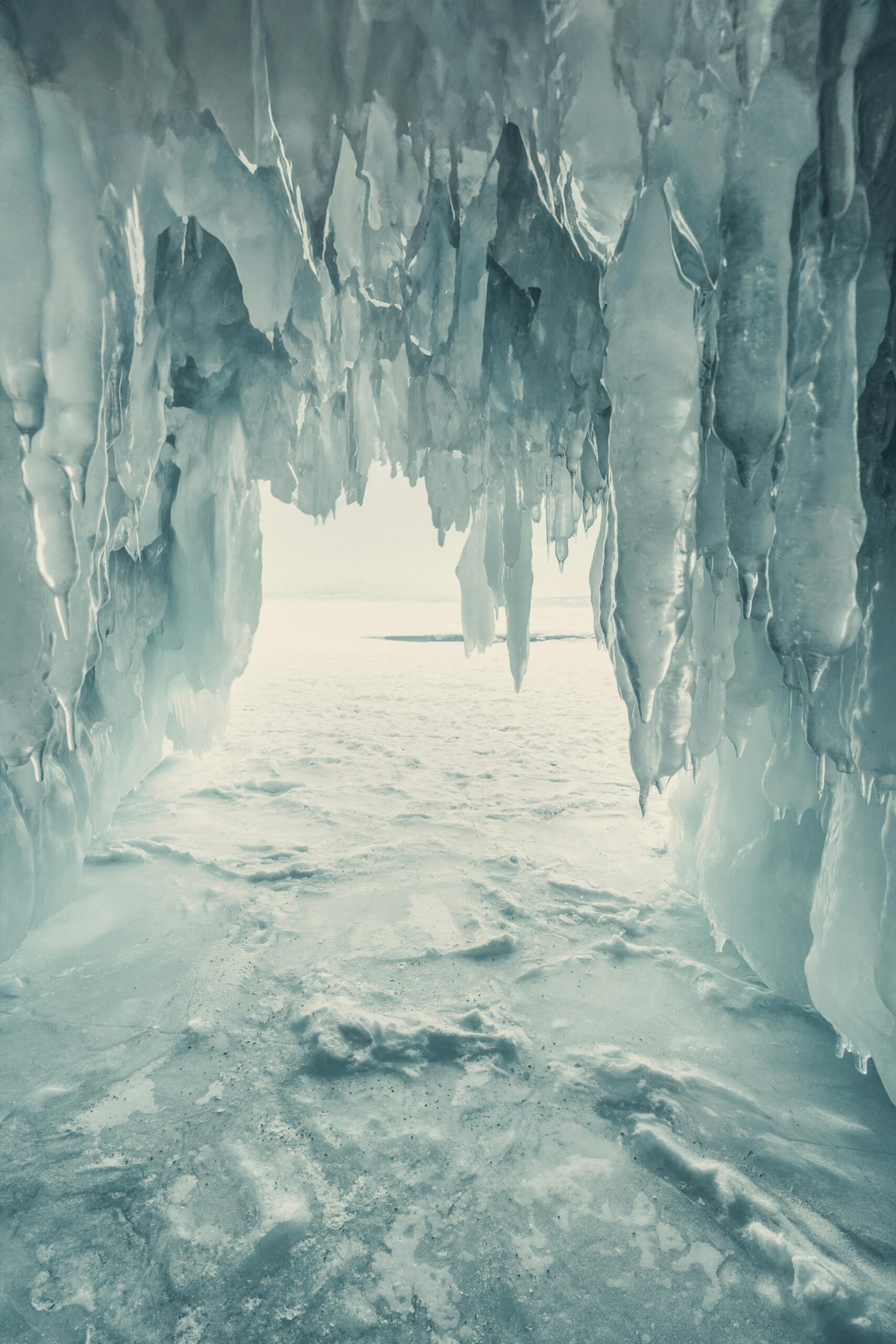 Interior of an icy cave with hanging icicles opening out to a bright, snow-covered landscape.