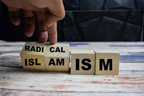 Wooden blocks spelling “Radical Islamism,” with a hand repositioning one block on a table.