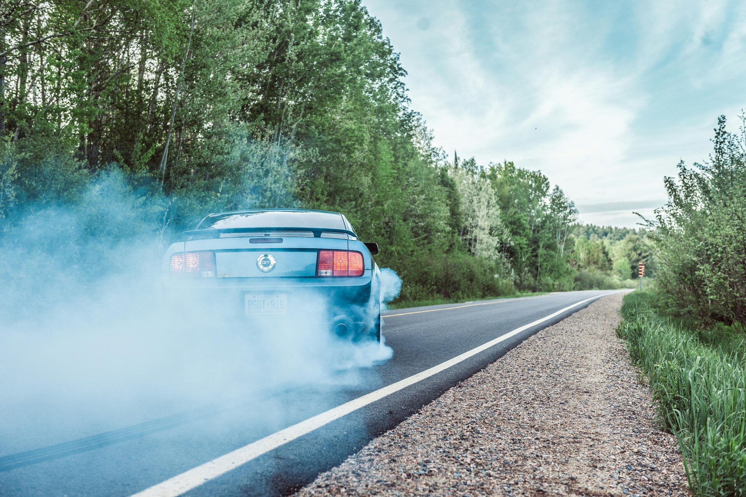 A blue sports car accelerating down a rural road, leaving a cloud of tire smoke behind it.
