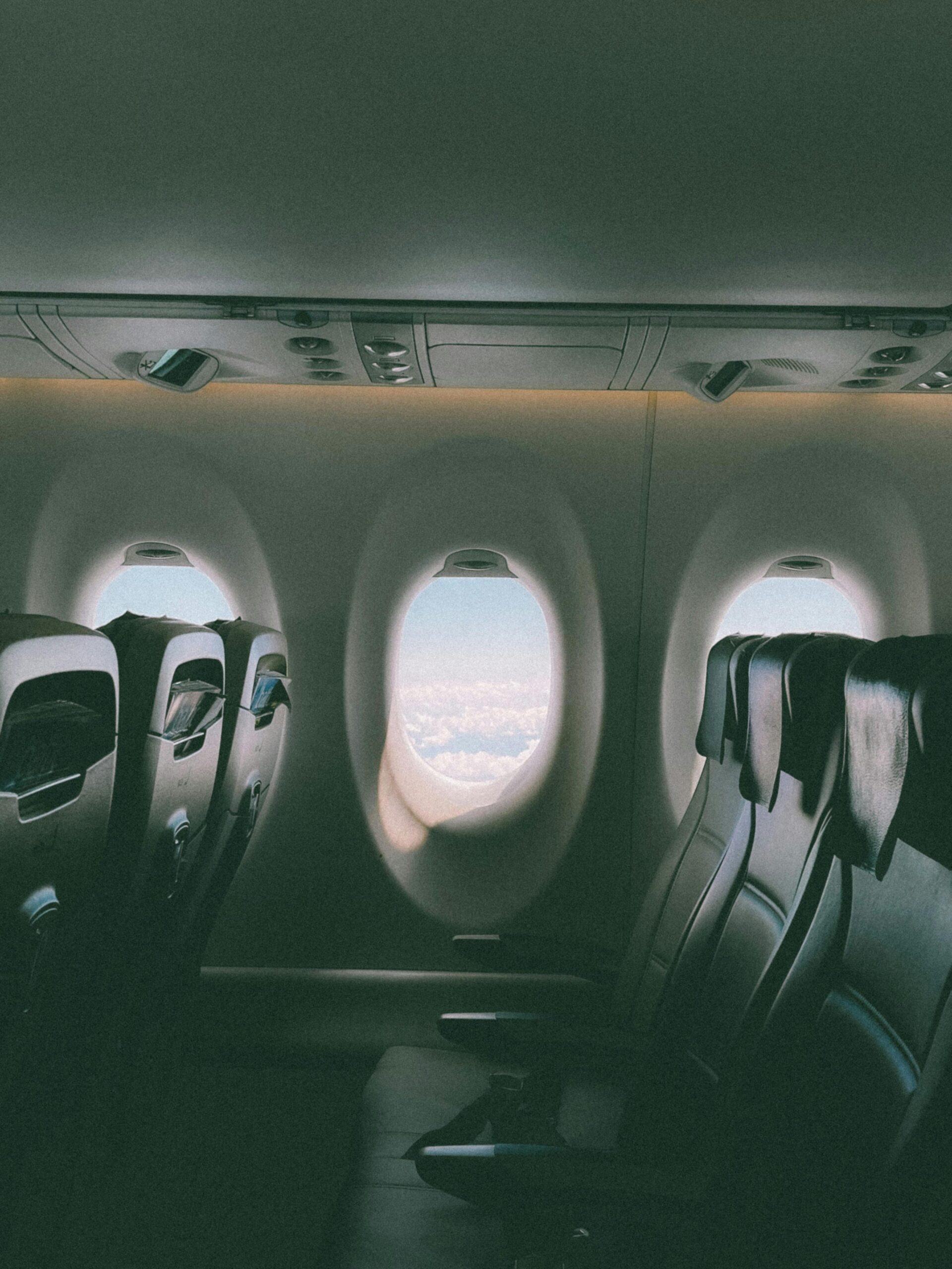 Empty airplane seats with sunlight coming through airplane windows above the clouds
