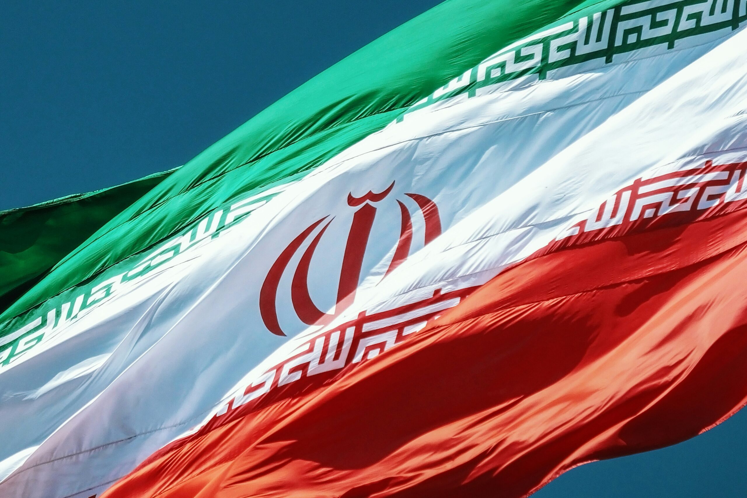 Iranian national flag waving in the wind against a clear blue sky.