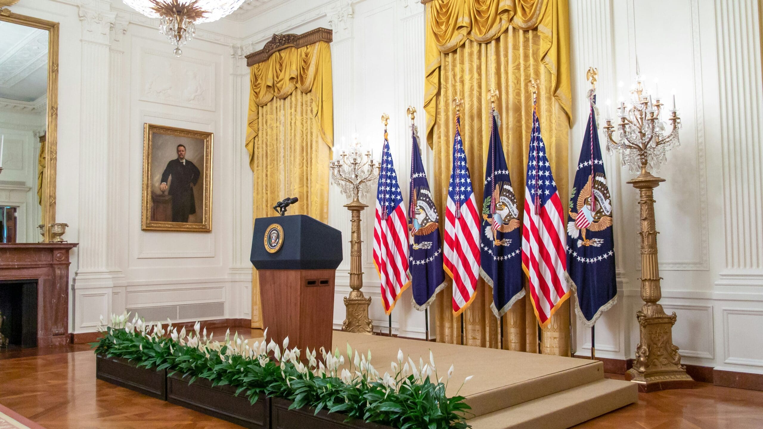 Empty presidential podium flanked by American flags in a formal White House setting