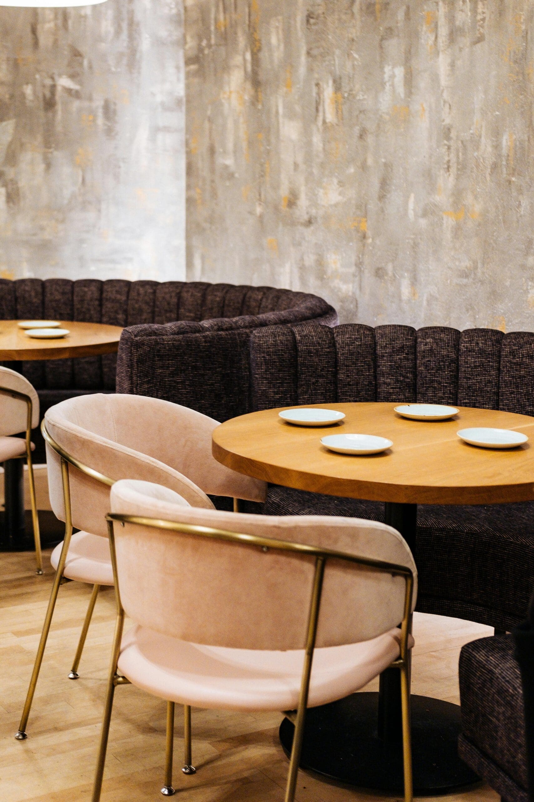A stylish, empty restaurant booth with velvet chairs, wooden table, and minimalist place settings.